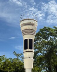 The station's Tempest sensor on its white pole, against a blue sky with trees behind